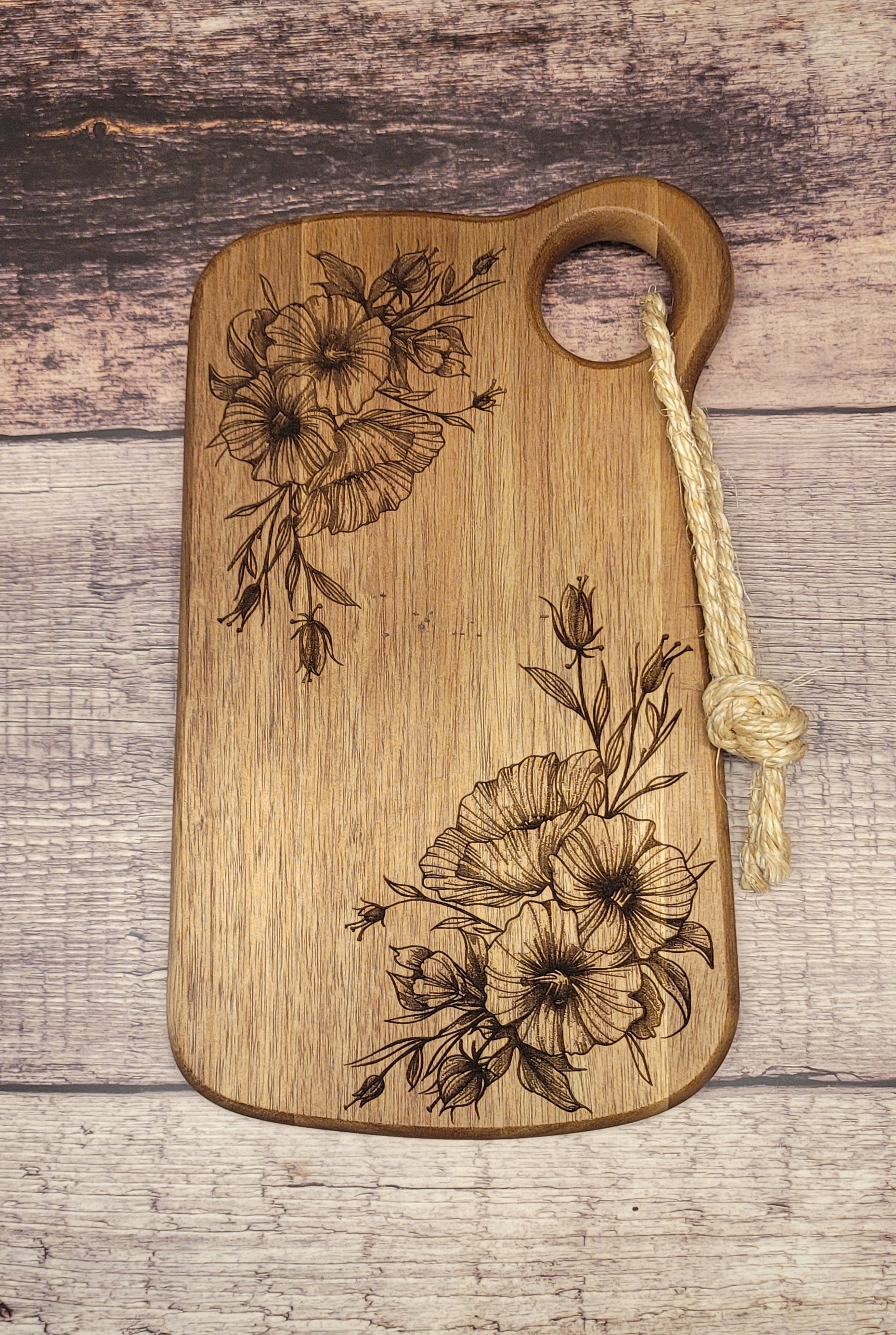 Acacia wood serving board with laser-engraved floral design and rope handle