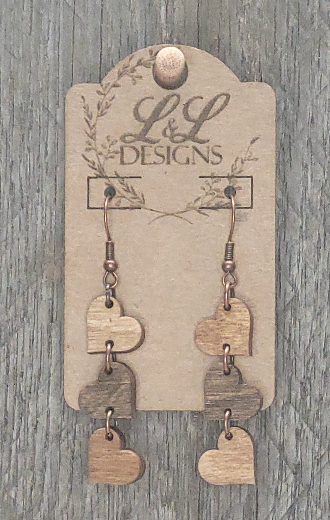 Three-tier heart wood earrings in natural finish displayed on L&L Designs branded card against weathered wood background