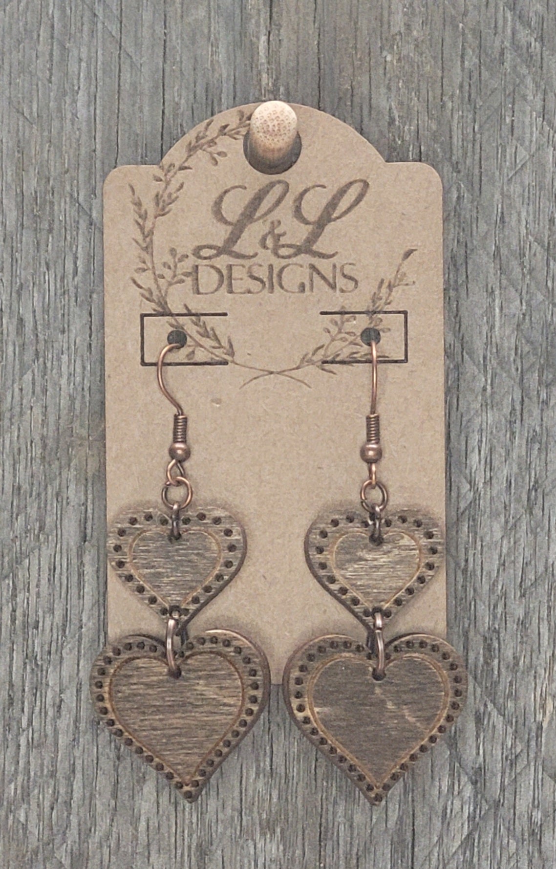 Two-tier heart wood earrings with intricate dotted border detail displayed on L&L Designs branded card against weathered wood background