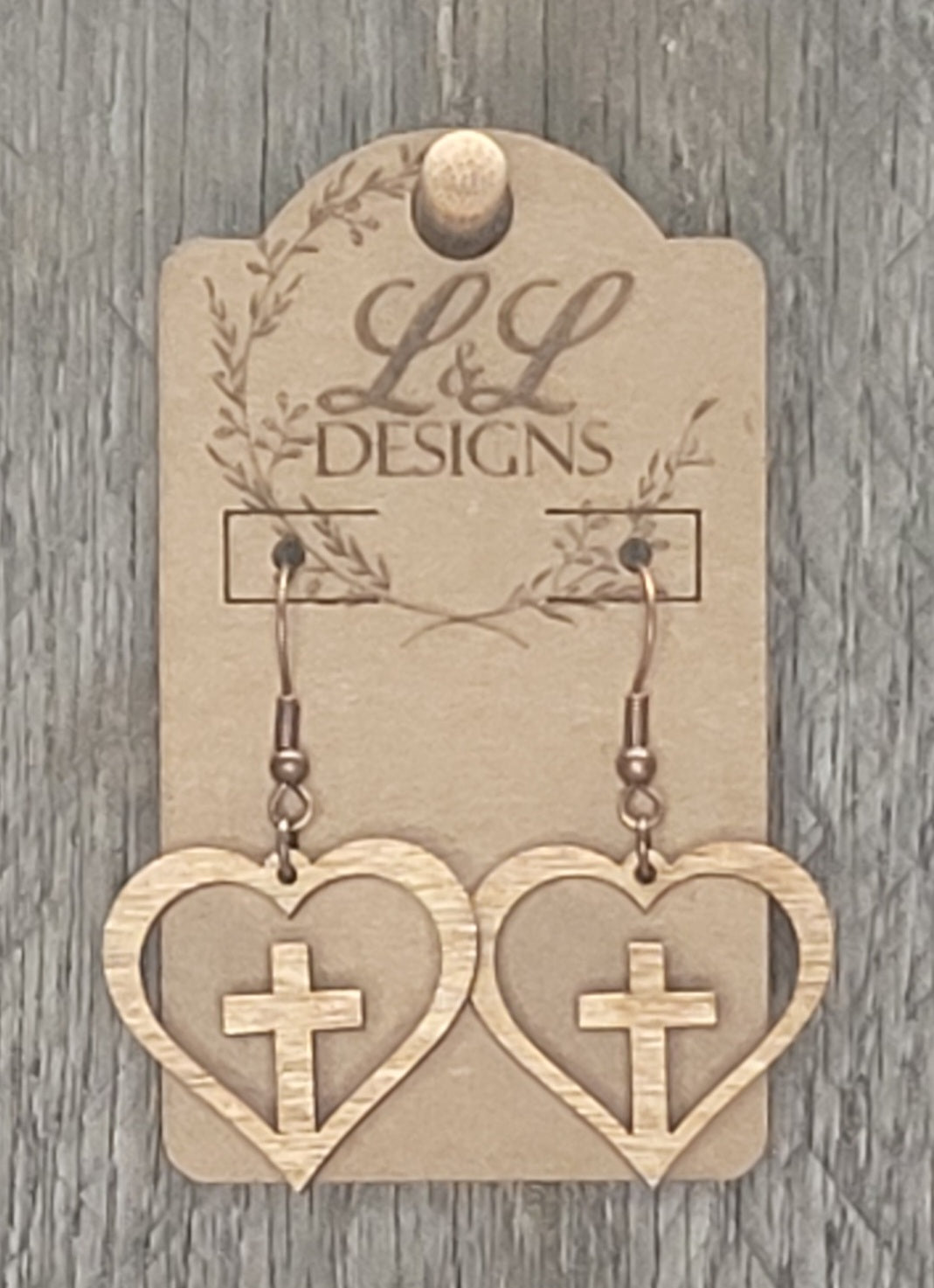 Heart-shaped wood earrings with cross cutout design displayed on L&L Designs branded card against weathered wood background.