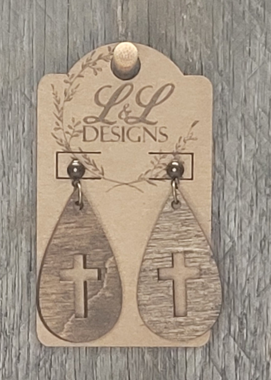 Teardrop-shaped wood earrings with cross cutout design displayed on L&L Designs branded card against weathered wood background.