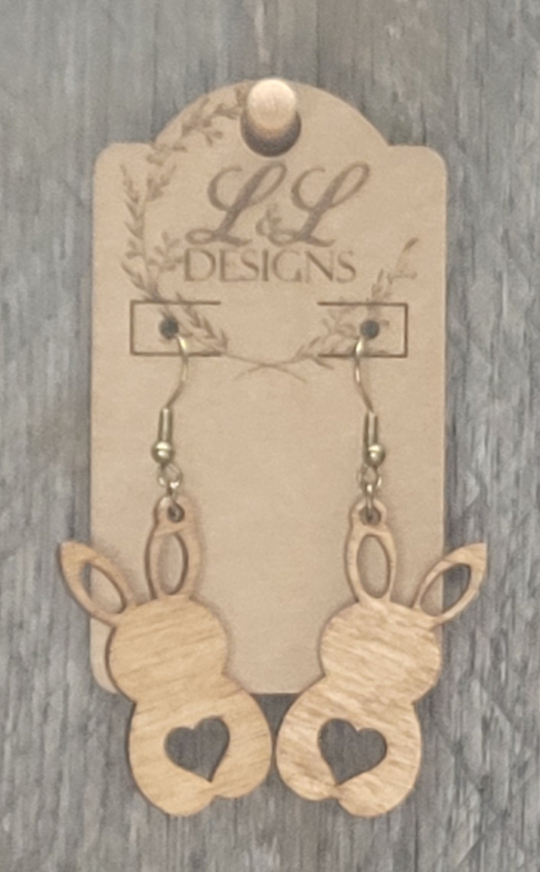 Bunny-shaped wood earrings with heart cutout design displayed on L&L Designs branded card against weathered wood background.