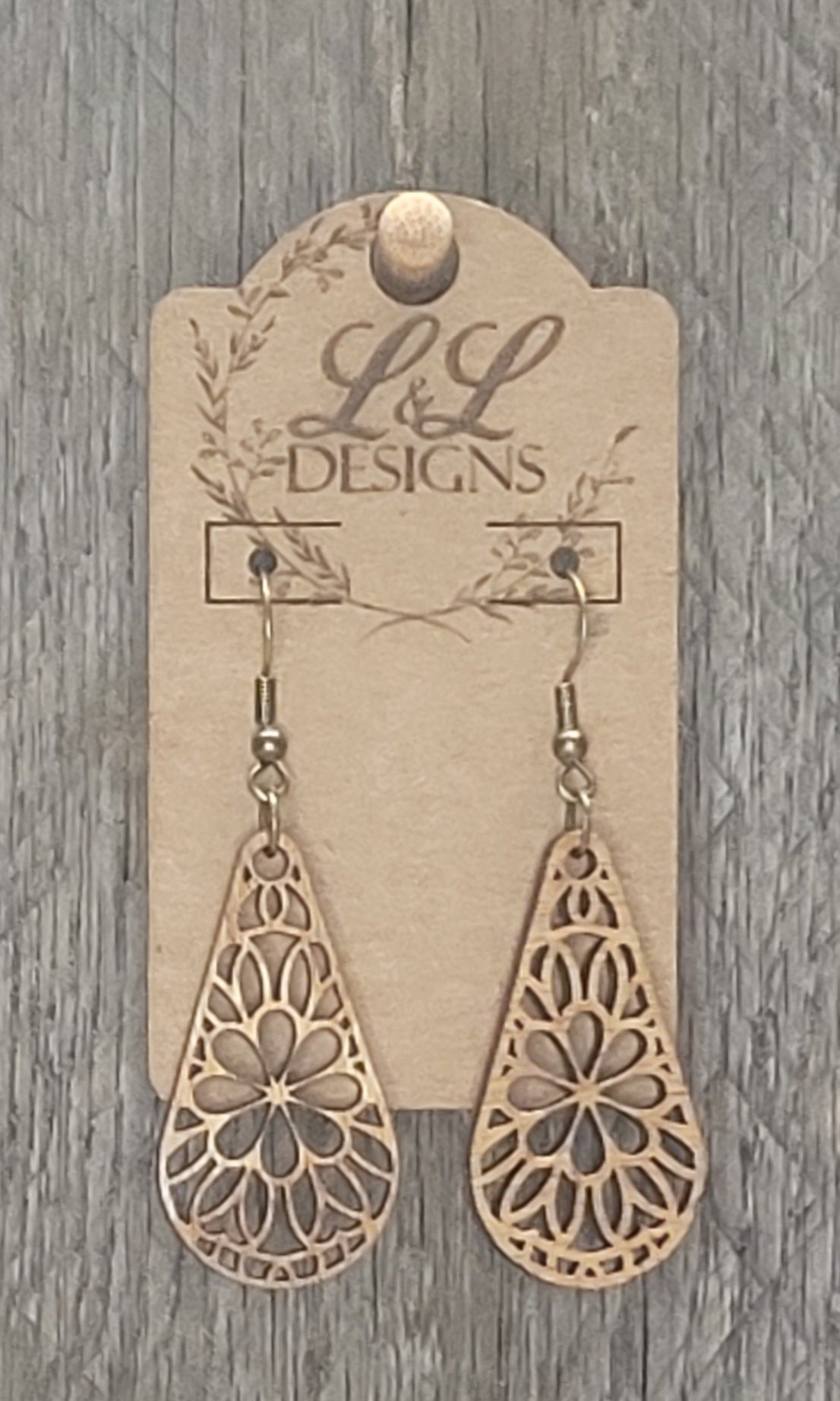 Teardrop-shaped wood earrings with intricate floral mandala cutout pattern displayed on L&L Designs branded card against weathered wood background