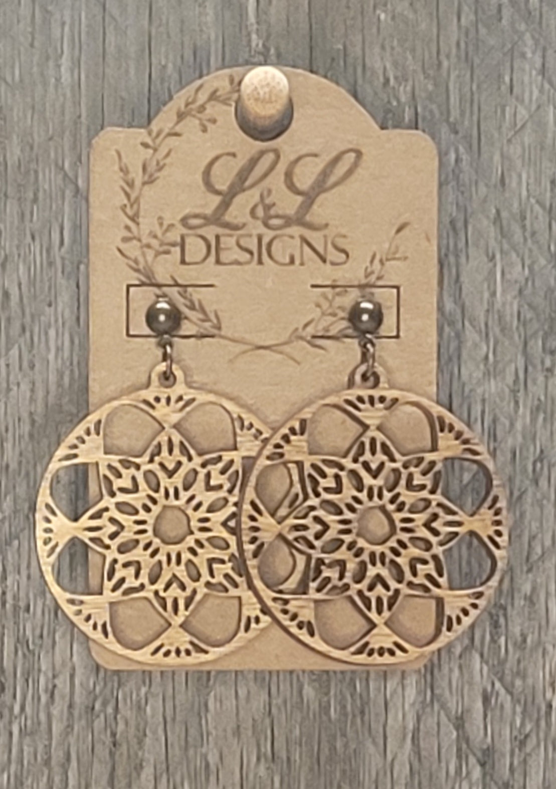 Circular wood earrings with intricate geometric mandala cutout pattern displayed on L&L Designs branded card against weathered wood background