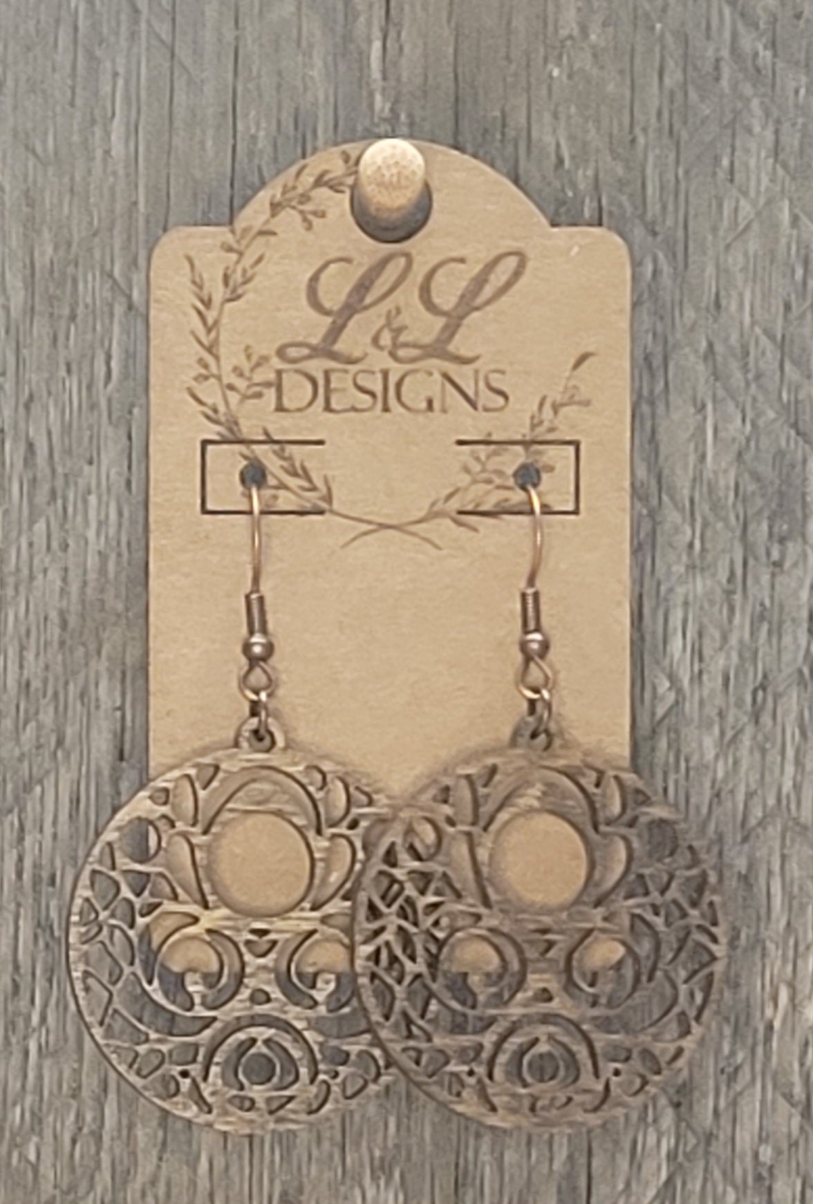 Circular wood earrings with ornate scrollwork and circle cutout pattern displayed on L&L Designs branded card against weathered wood background.