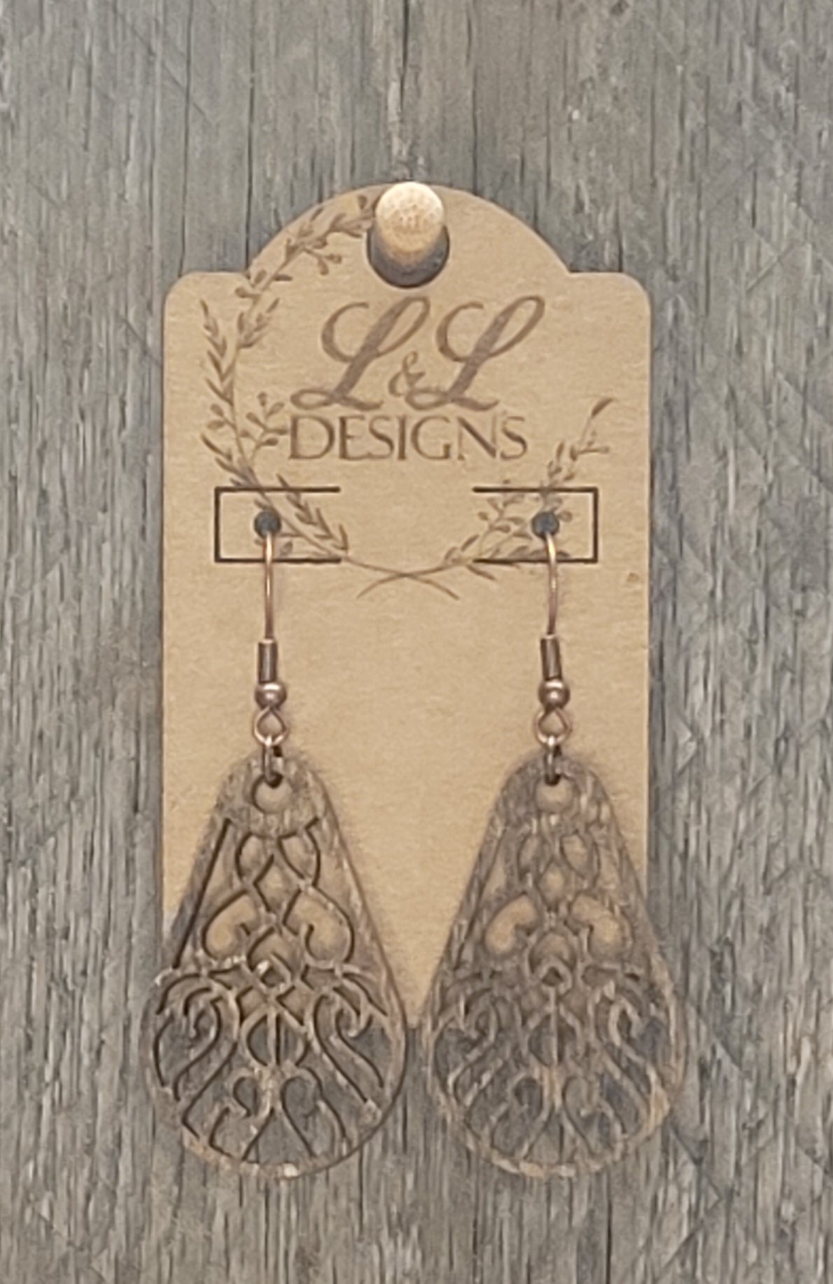 Teardrop-shaped wood earrings with ornate scrollwork cutout pattern displayed on L&L Designs branded card against weathered wood background.