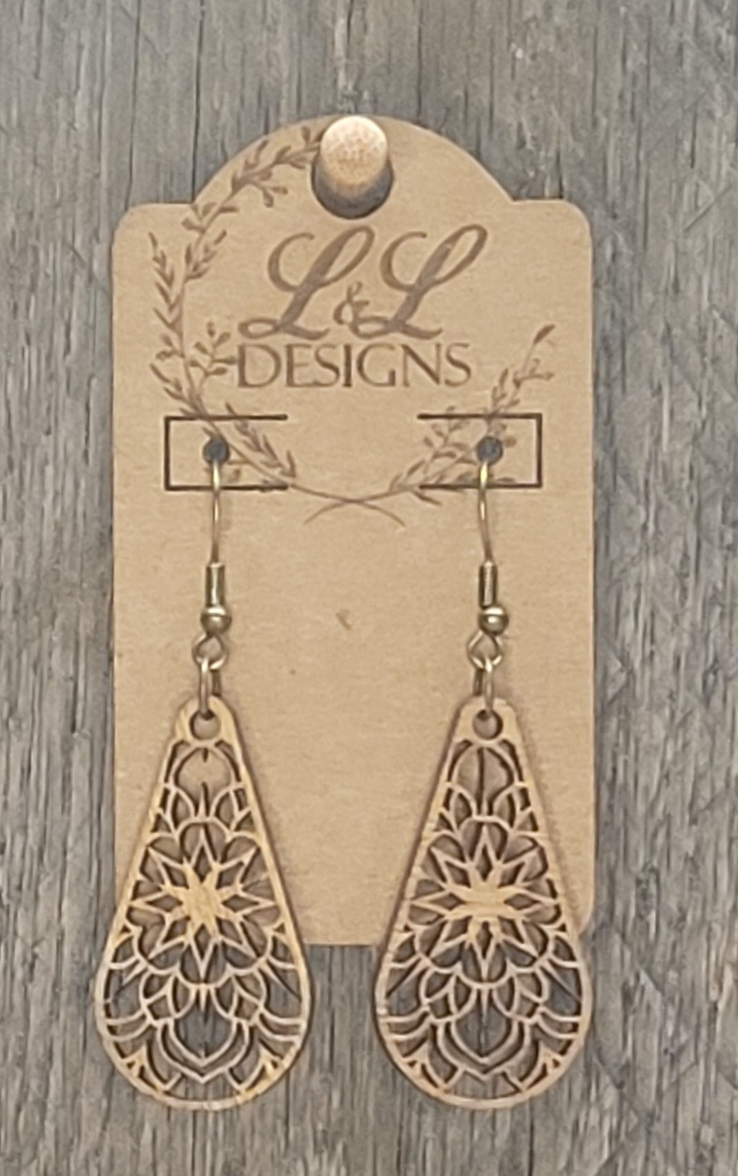 Close-up view of floral mandala teardrop wood earrings showing detailed laser-cut pattern on L&L Designs branded card against weathered wood background