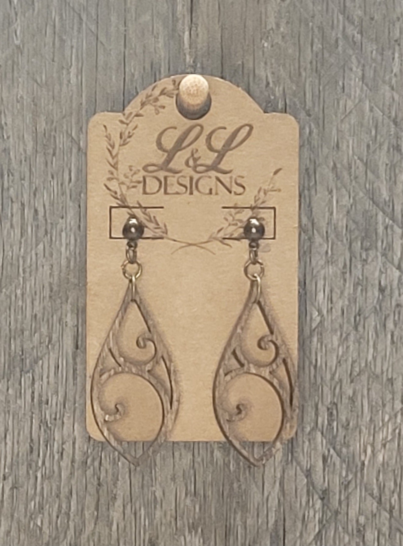 Teardrop-shaped wood earrings with swirl and circle cutout design displayed on L&L Designs branded card against weathered wood background.