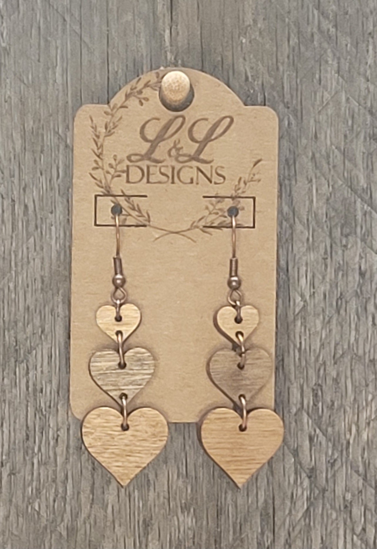 Triple heart cascade wood earrings with three connected hearts displayed on L&L Designs branded card against weathered wood background.