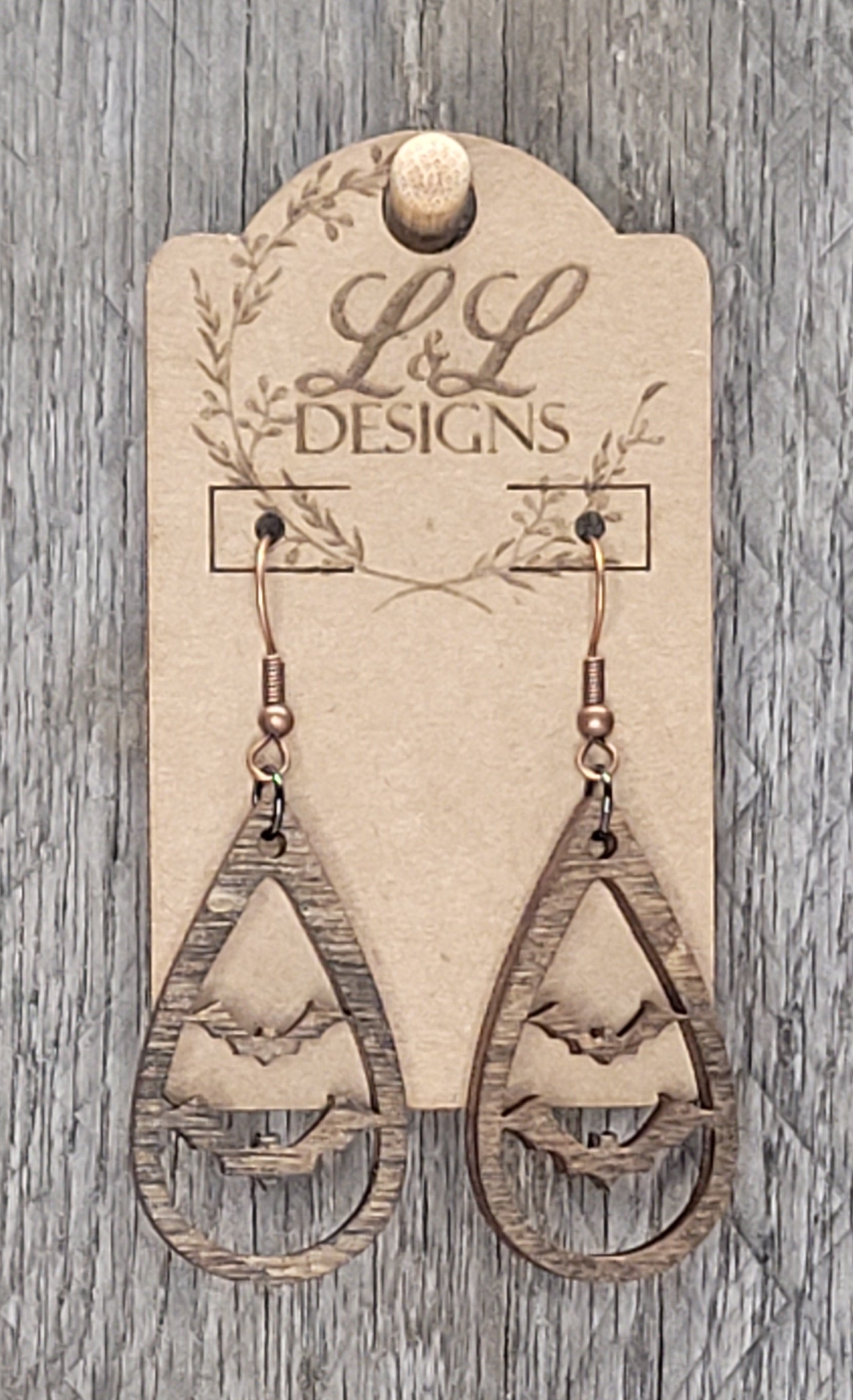 Teardrop-shaped wood earrings with bat cutout design displayed on L&L Designs branded card against weathered wood background.