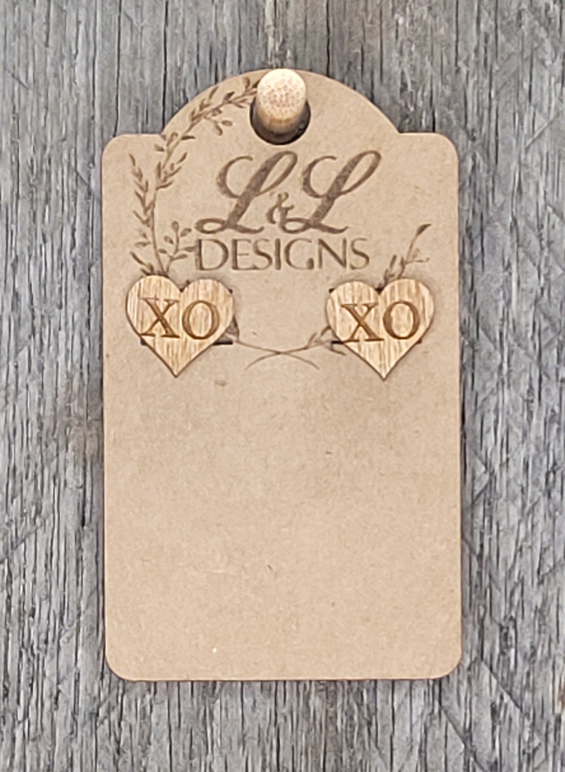 Heart-shaped wood stud earrings with 'XO' engraved message displayed on L&L Designs branded card against weathered wood background.