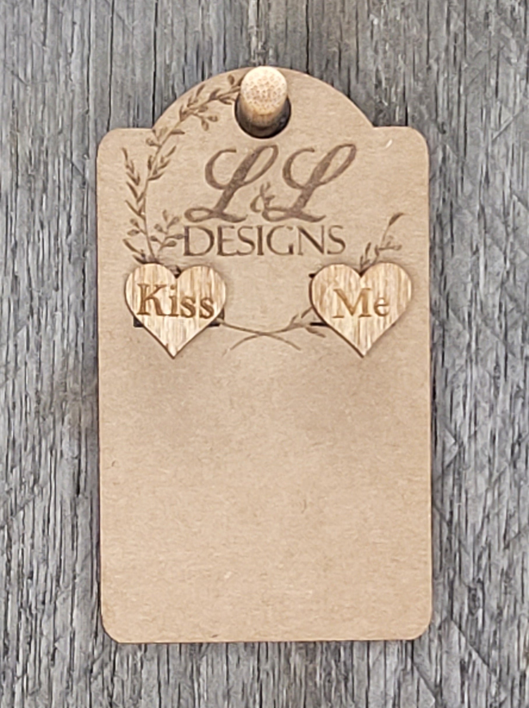 Heart-shaped wood stud earrings with 'Kiss Me' engraved message displayed on L&L Designs branded card against weathered wood background.